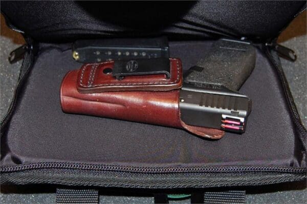 A gun and holster are sitting in the back of a suitcase.