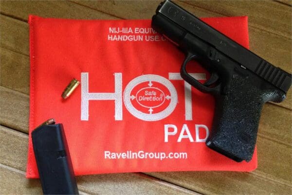 A gun and some other items on top of a red hot pad.